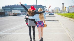 Blonde and brunette girl walking with their arms around each other and arms in the air