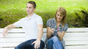 Girl picking the petals off flowers to see if guy likes her while guy has his back turned away from her