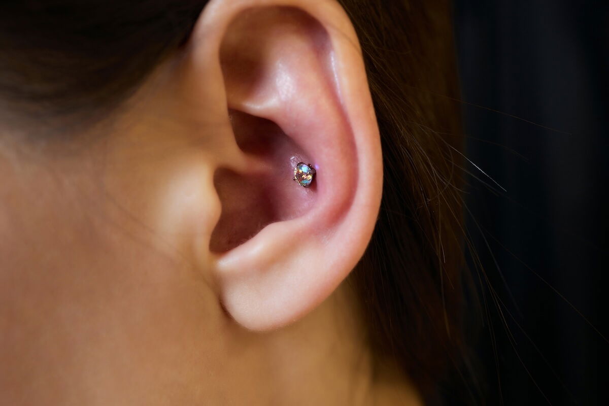 Woman with gem conch piercing inside ear: Shutterstock. piercings on an ear. Conch and helix piercings close up.